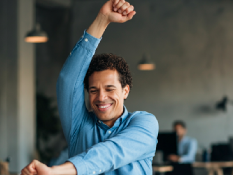 A cheerful office worker taking a stretching break in a modern workspace