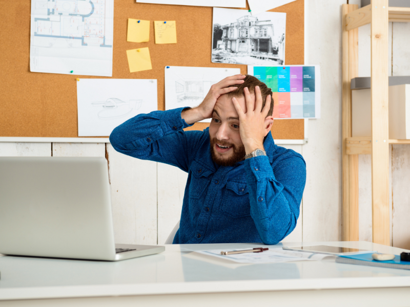 A young man looking stressed as he stares at his laptop.