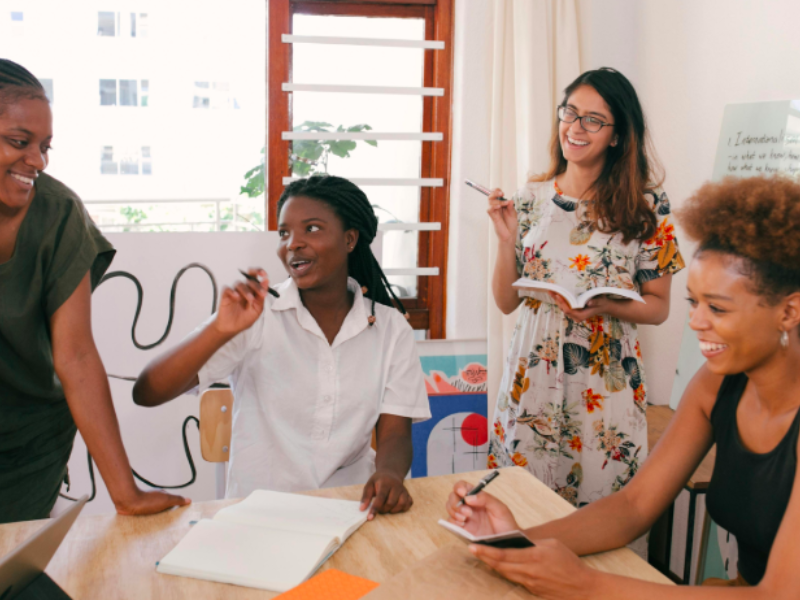 Four women actively collaborate and brainstorm around a table, smiling and engaged in discussion.