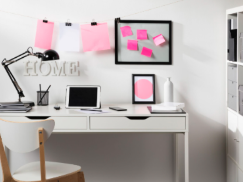 A bright, modern home office with a white desk, chair, and shelving unit, decorated with pink accents