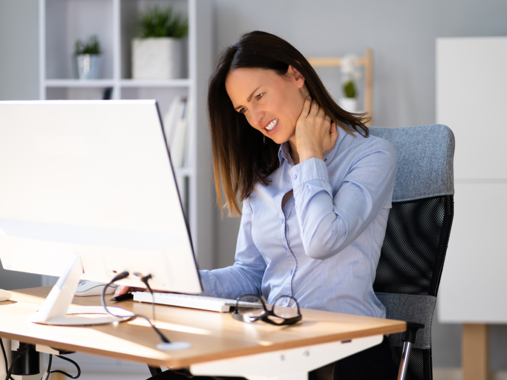 A person hunched over a desk with poor posture, rubbing their neck or back.