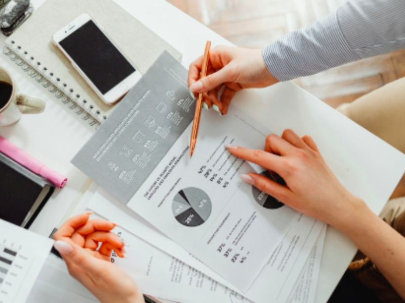 Close-up of hands with a pen pointing to charts on a document, with a phone and coffee nearby.