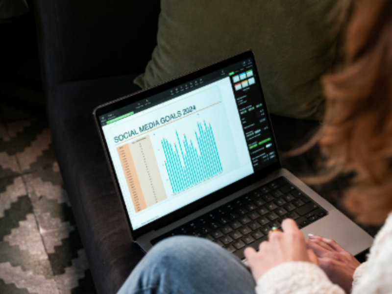 A person sitting on a couch with a laptop resting on their lap, the screen illuminated with a website or document containing charts and graphs.